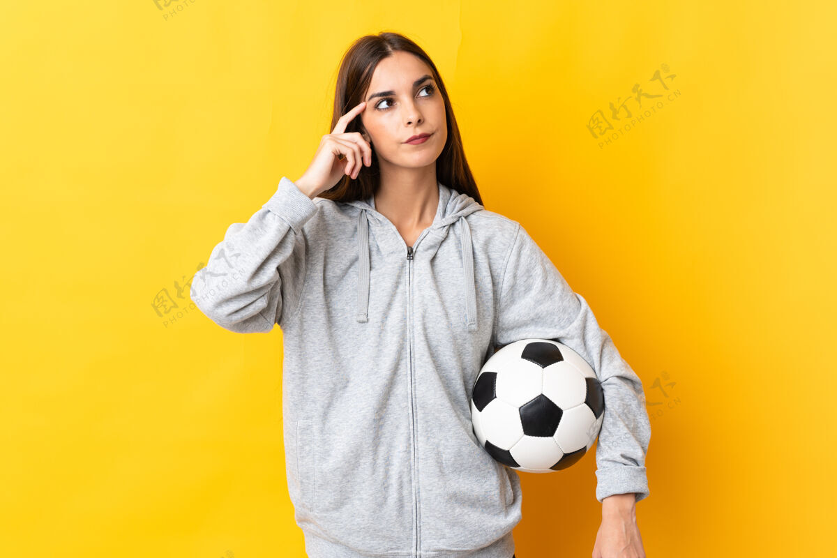 年轻年轻的足球运动员女人孤立在黄色的背景有疑问和思考年轻困惑女人