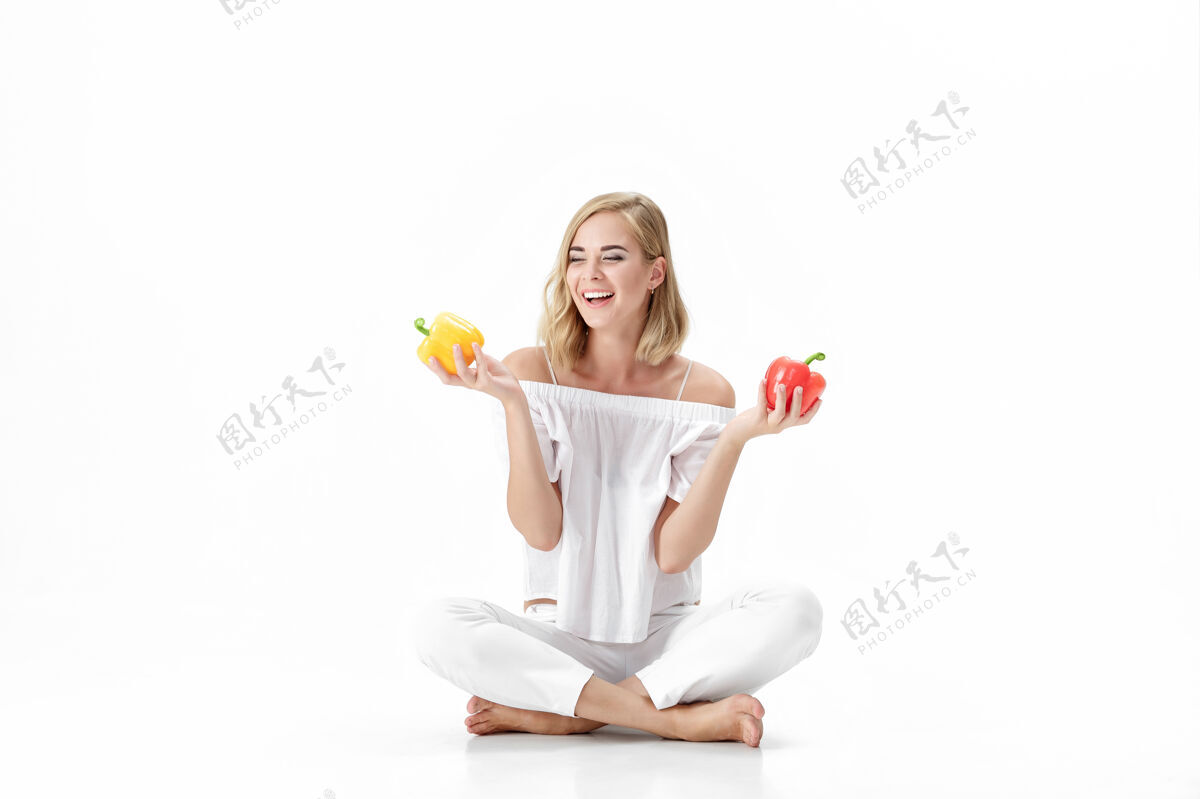 举行美丽的金发女人 穿着白色上衣 手里拿着黄色和红色的铃铛胡椒粉健康节食和节食新鲜性感快乐
