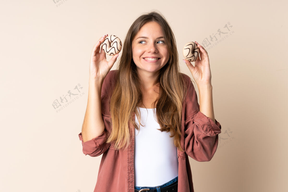 食物年轻的立陶宛女人拿着甜甜圈被隔离在米色背景下面包店金发女孩