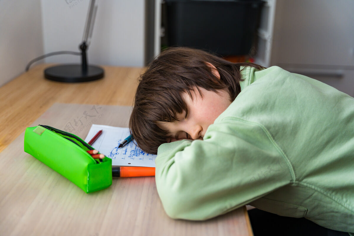 书房十岁的小男孩坐在桌子旁做作业回家累了孩子睡觉的时候在课桌上做运动室内注意力集中疲倦