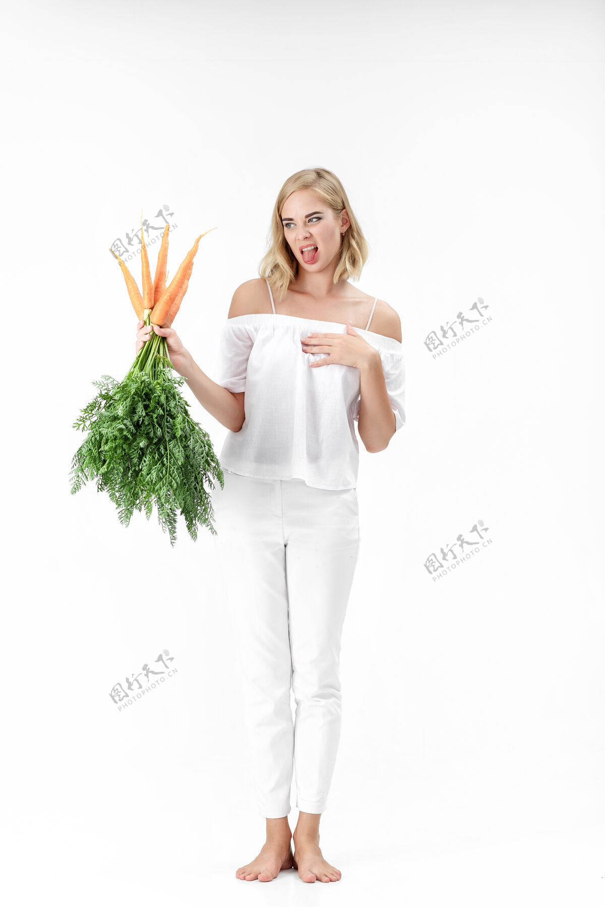 维生素一个穿着白衬衫的金发女人 手里拿着一根白衬衫上有绿叶的胡萝卜背景女孩吃胡萝卜和节食的感觉不好蔬菜美丽美丽