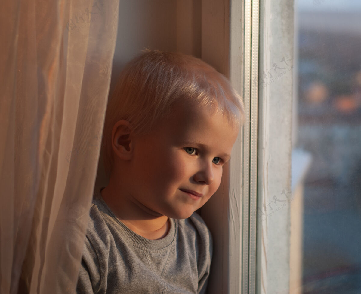 窗口夕阳下窗边一个男孩的画像孩子特写脸看