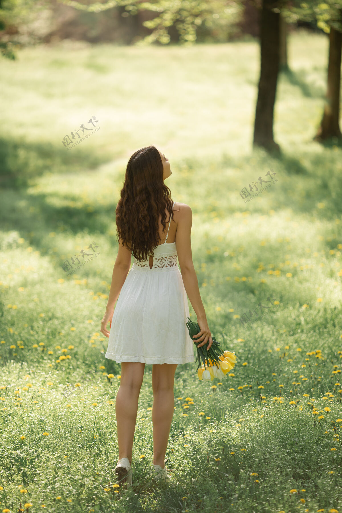 女士后视图：一位身着白色连衣裙的迷人女士 迎面走来一束春花化妆花束花园