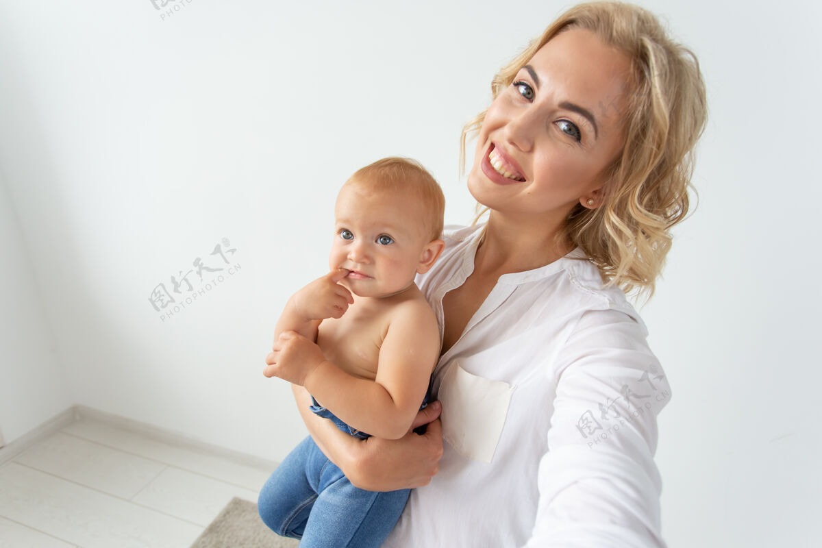 可爱家庭和母亲的概念-快乐年轻的金发妈妈与小宝宝自拍拍照房子单身