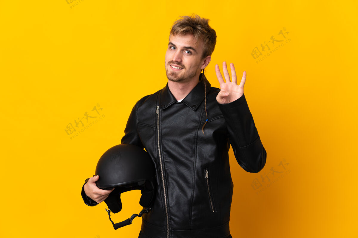 摩托车一个戴着摩托车头盔的男人在黄色的地上快乐地数着四个手指司机帅哥摩托车手