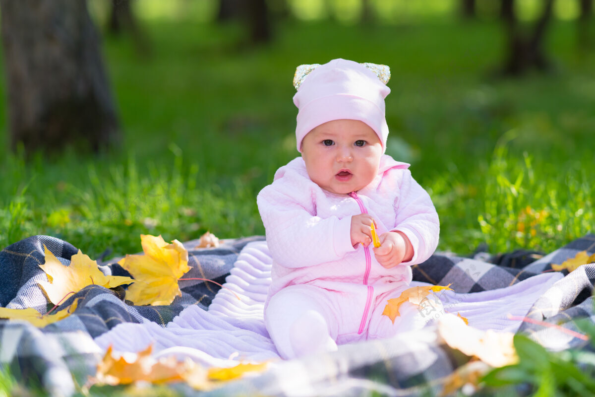 女儿公园里 一个穿着粉红色衣服的婴儿在秋叶间的野餐地毯上玩耍新生儿郁郁葱葱年轻