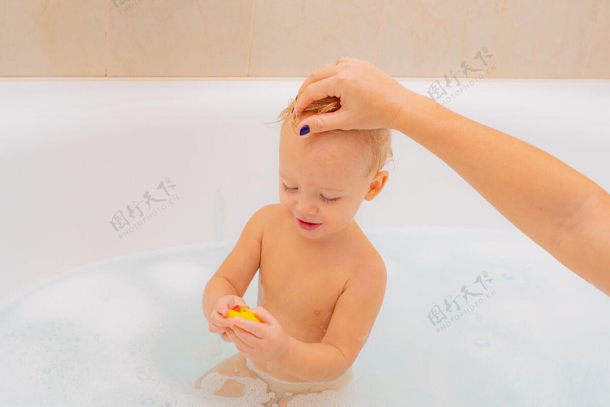 头发1岁婴儿在浴室洗澡淋浴小好奇漂亮的婴儿坐在白色的浴室里 湿漉漉的泡沫头发看起来远离健康孩子们浴缸浴衣婴儿