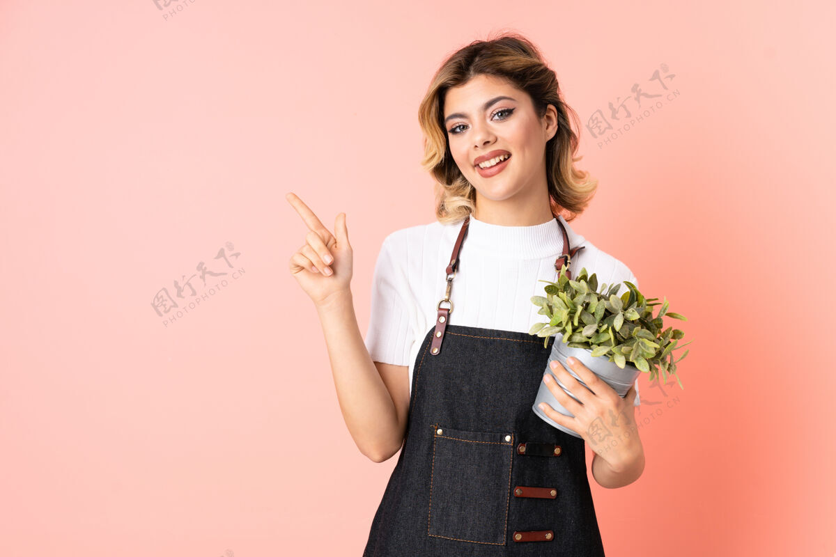 产品俄罗斯园丁女孩拿着一株孤立的植物用手指指着粉色的一边成长花盆花园