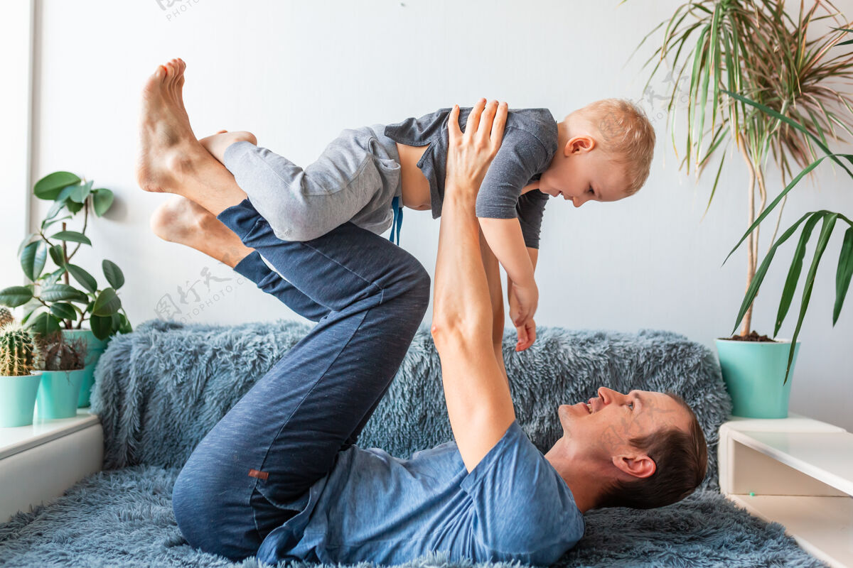 家庭快乐的男婴飞在爸爸怀里看 慈爱的爸爸抱着可爱的小儿子在沙发上玩飞机 亲热 开心飞机快乐休闲