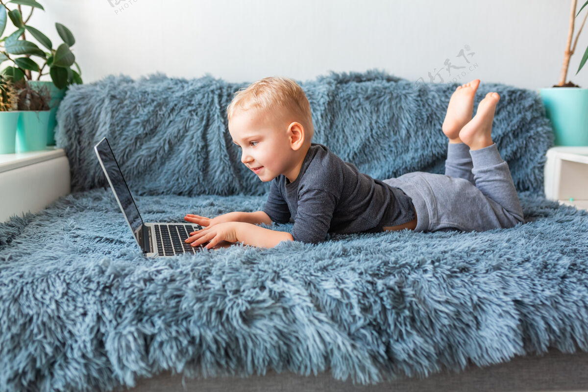 视频通话小男婴躺在沙发上玩笔记本电脑电子学习 远程学习 远程交流的概念学习科技男孩