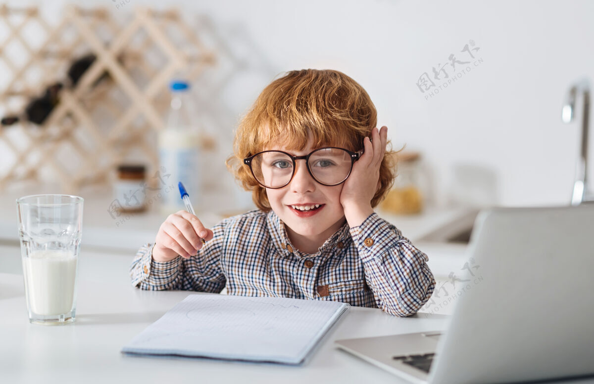 学习像个聪明人盖伊开朗决心迷人的孩子戴着可爱的眼镜 一边学习 一边坐在白色的桌子旁生姜识字眼镜