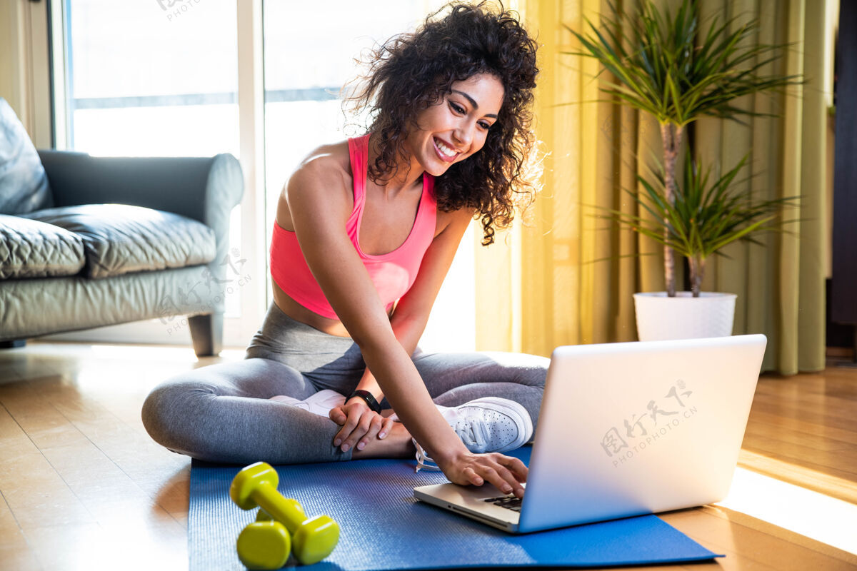 网络研讨会穿着运动服的运动型女人坐在客厅里 手里拿着哑铃 手里拿着笔记本电脑室内房间健身房