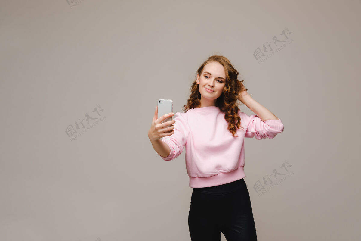 运动一个微笑的快乐女孩穿着粉色上衣 在灰色的手机上自拍小玩意生活方式休闲