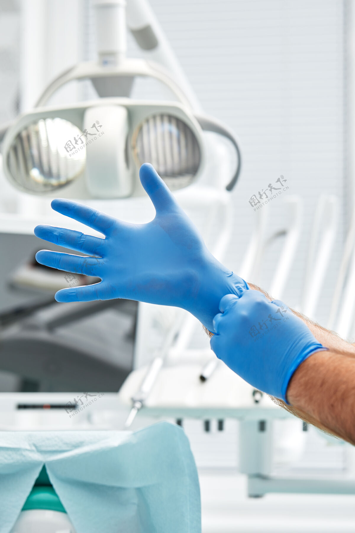 工作一位女牙医戴上手套 以牙科办公室的牙科设备为背景 这是一个快乐的病人和牙医概念护士手套蓝色