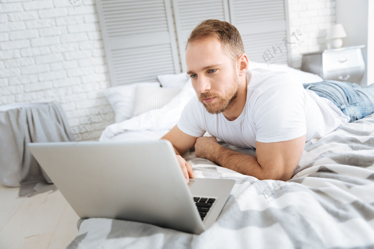 积极性享受我的周末很高兴运动迷人的男人躺在床上 一边用笔记本电脑表达兴趣网络内部发展