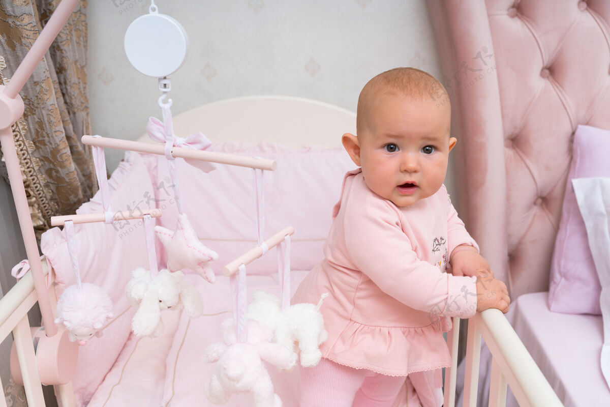 颜色一个快乐 好奇的婴儿在一个粉红色的婴儿床和卧室场景与悬挂的手机小新生儿天真