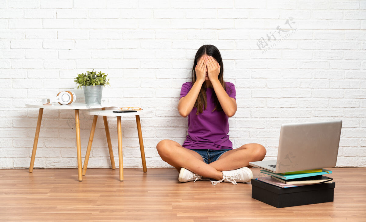 黑发坐在室内地板上拿着笔记本电脑用手捂住眼睛的年轻女子地板隐藏个人电脑