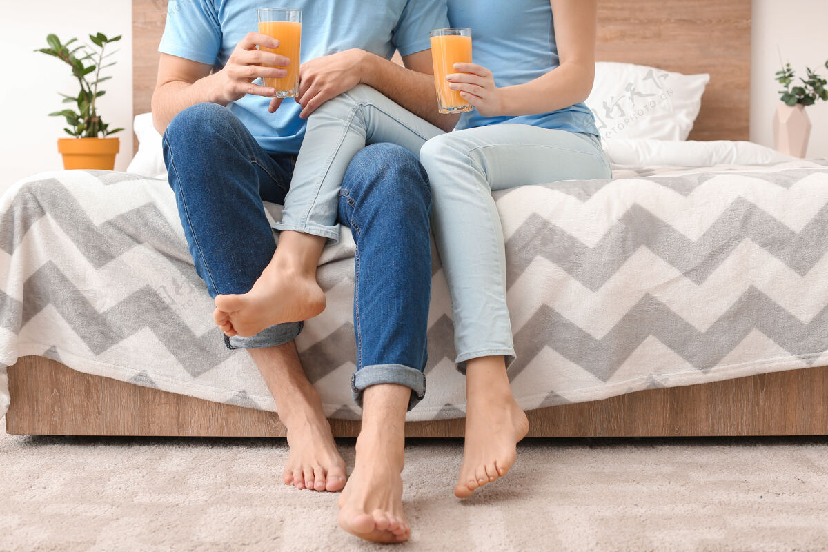 女人一对喝着果汁的年轻夫妇坐在家里的床上早餐床赤脚