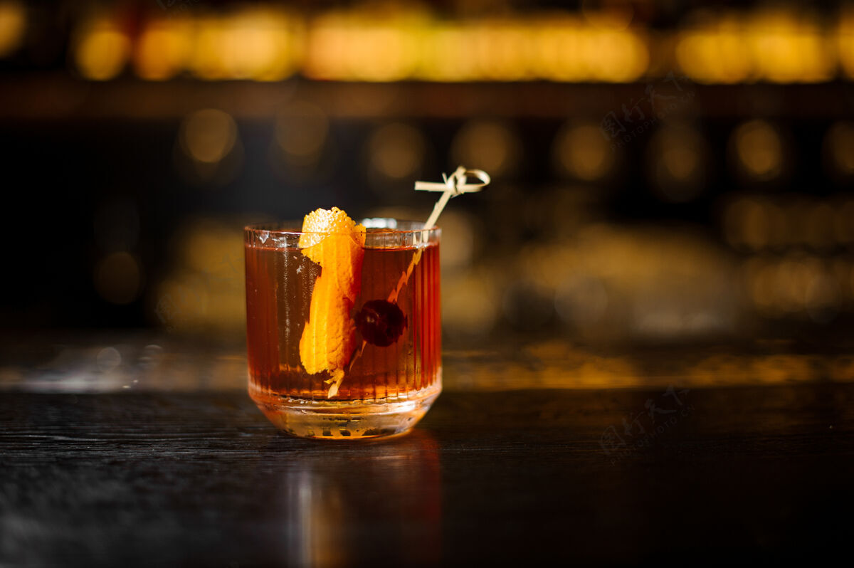 手吧台上摆着一杯用橘皮和樱桃装饰的威士忌鸡尾酒冰饮料新鲜
