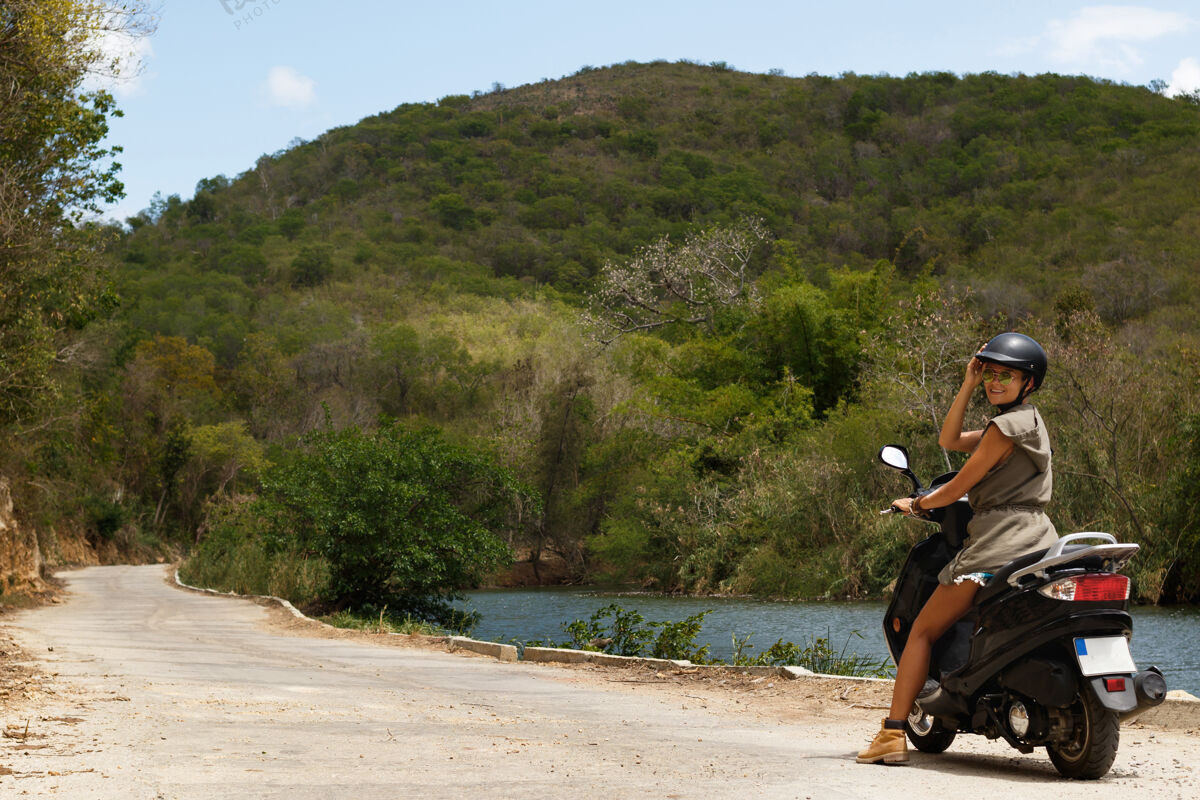 放松年轻的女旅行者在山里的乡村老路上开着摩托车休闲安全旅行