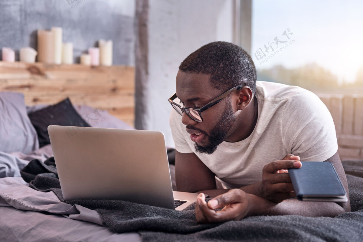 室内工作地点家乡非洲年轻人戴着眼镜 在家里用笔记本电脑工作年轻自由职业者严肃