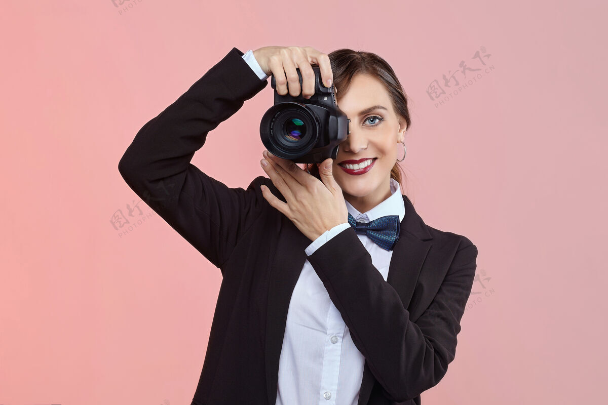 女人漂亮的女摄影师在一个男人的西装和复古发型的粉红色背景自信背景快照
