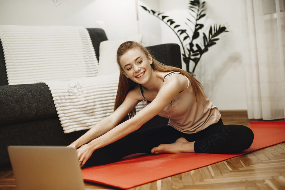 微笑一幅迷人的女人在家做伸展运动的画像 她在地板上看笔记本电脑上的教学视频健身房垫子活跃