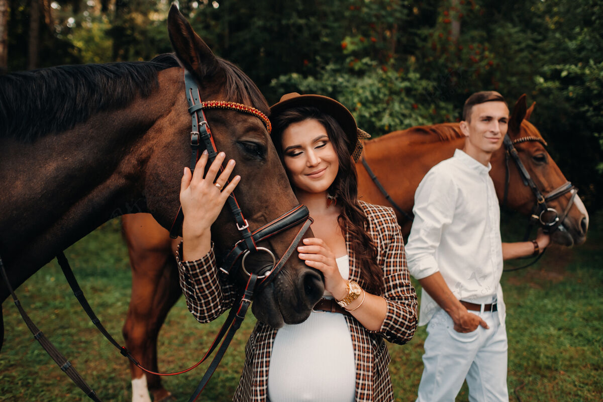 等待在大自然的森林里 一个戴帽子的孕妇和一个穿白衣服的男人站在马旁边动物女人腹部
