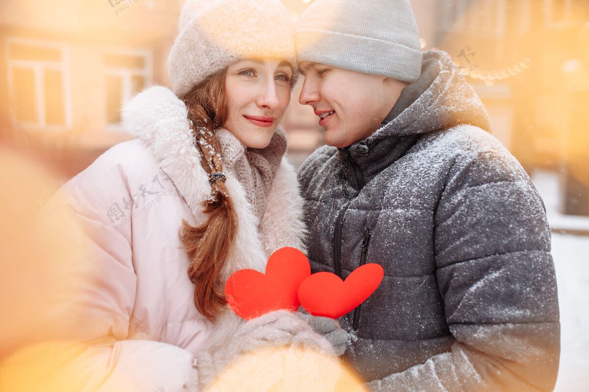 男人冬日里 一对年轻的情侣捧着红色的纸心 在外面感受着快乐和幸福爱情浪漫男人和女人在公园的雪下庆祝情人节享受手套惊喜