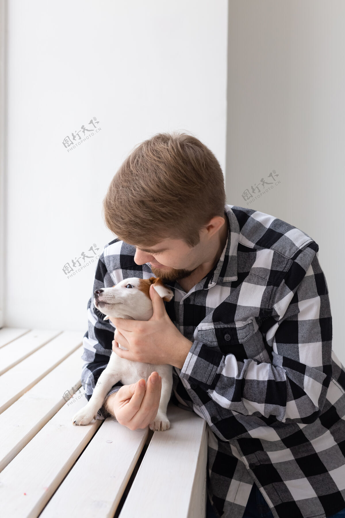 动物人 宠物和动物的概念-年轻人拥抱杰克罗素梗小狗附近的窗口白色成人狗年轻