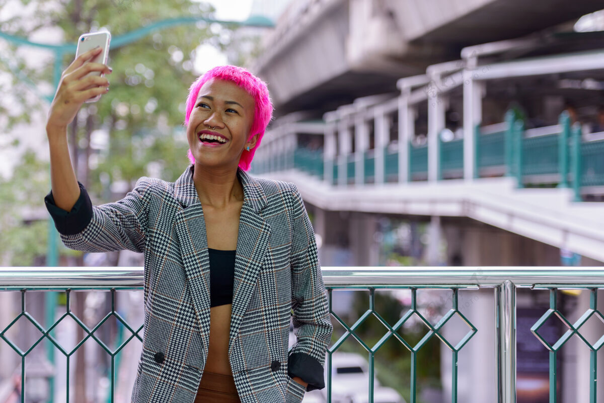 影响者年轻叛逆的亚洲女商人的肖像 粉红色的头发在城市户外的人行天桥上个人古怪公司