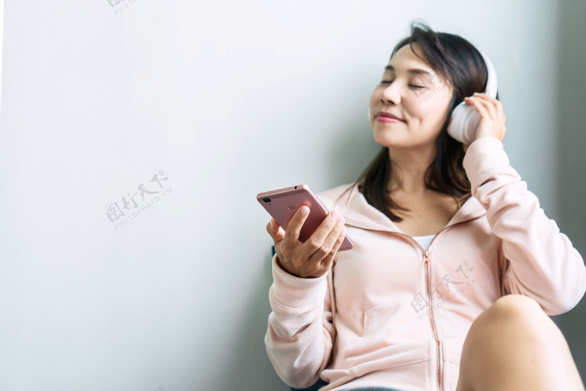 耳机年轻的亚洲女人坐在沙发上听音乐人微笑女孩