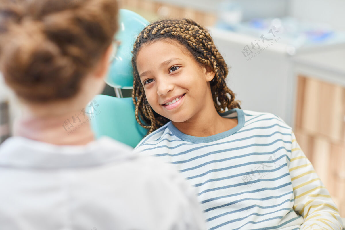 孩子微笑的小女孩坐在牙科椅上和医院的医生交谈肖像微笑牙医办公室