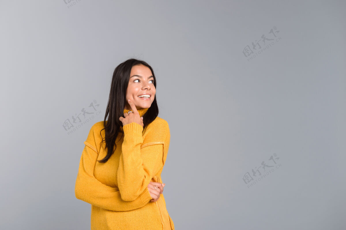 快乐一位身着毛衣 面带微笑的年轻女子孤零零地站在灰色的墙上 望着远方手表情吸引力