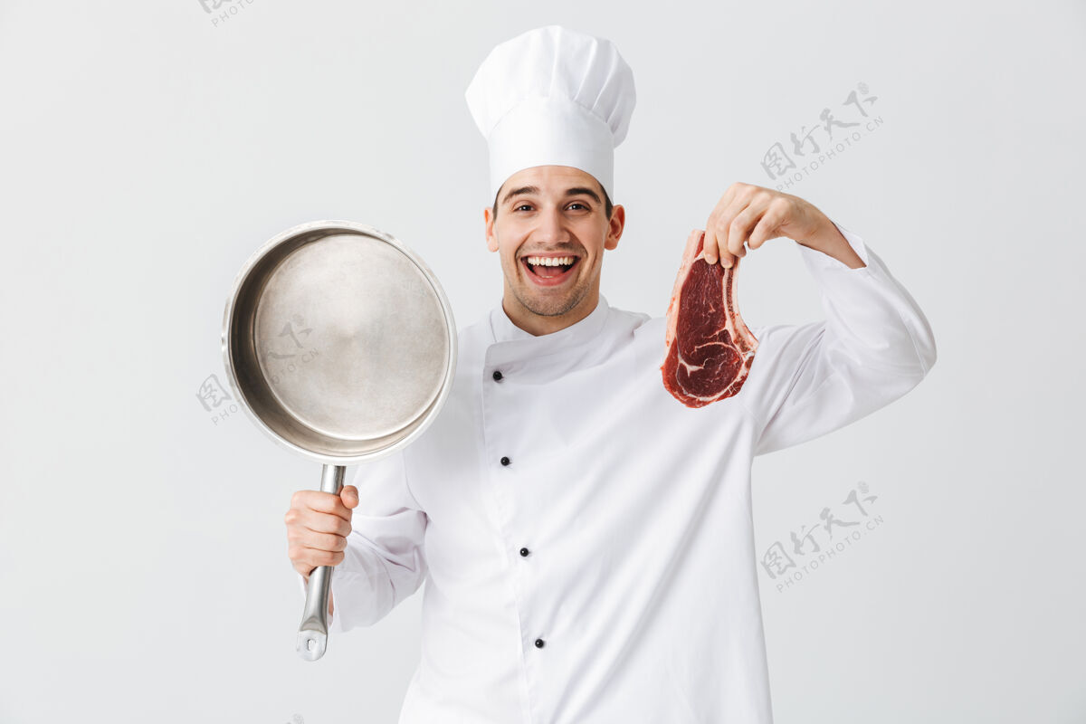 准备开朗的厨师穿着制服展示生牛排拿着煎锅隔着白墙食物切片烹饪