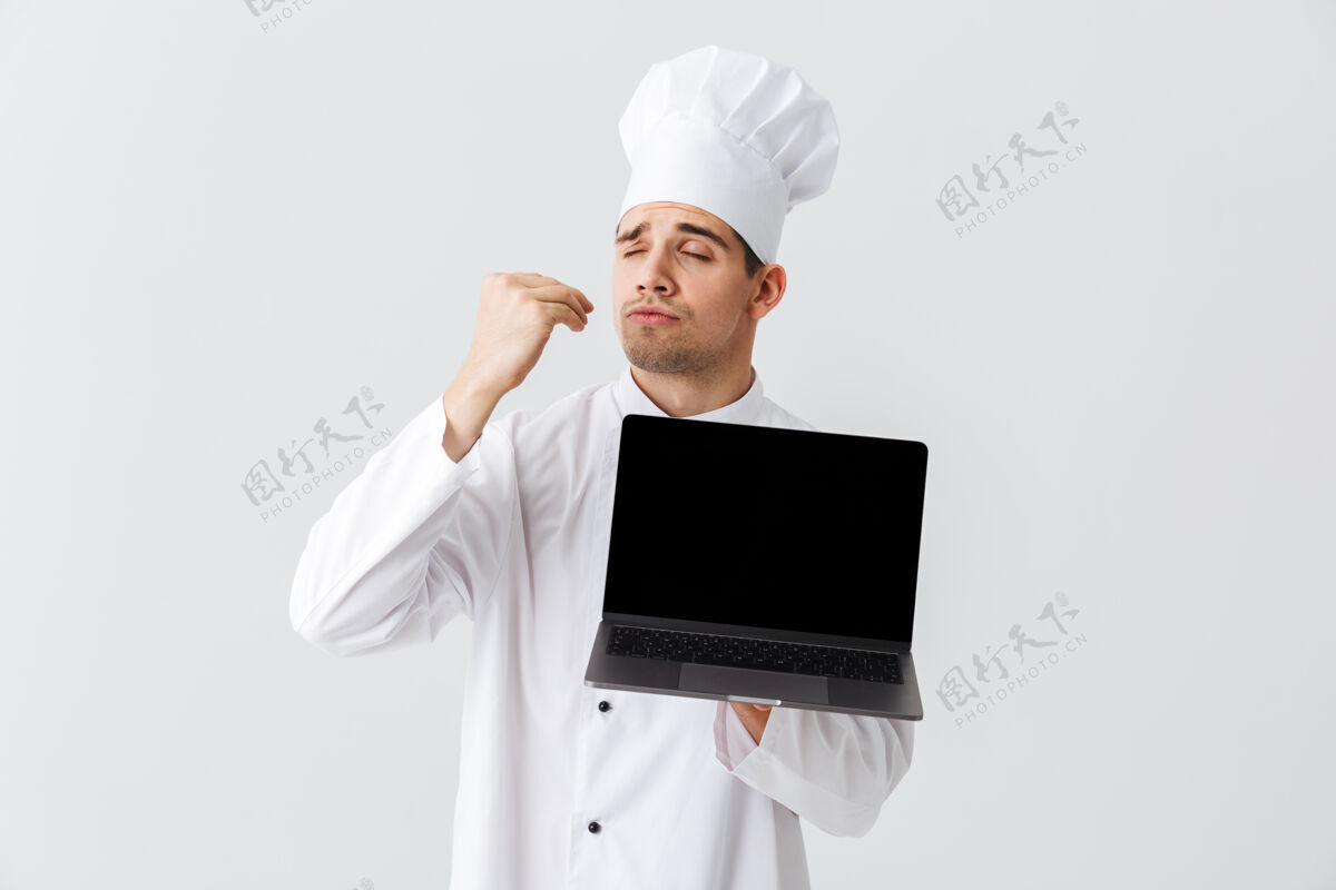 便携式开朗的厨师身穿厨师制服站在白色的墙上 手里拿着银行屏幕的笔记本电脑帅气工人职业