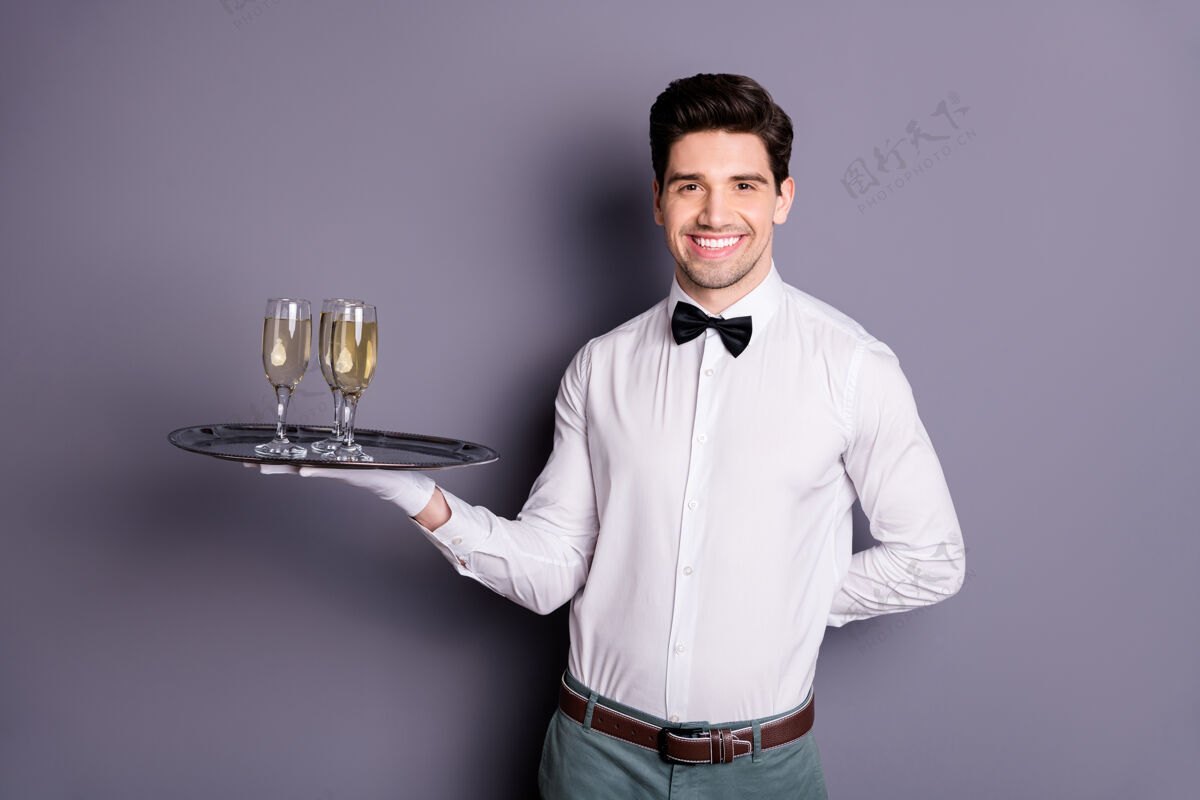 手套正面欢快的肖像餐厅职员服务员端着酒盘给客人点菜穿白衬衫黑蝴蝶结隔着灰色的墙制服鞠躬微笑