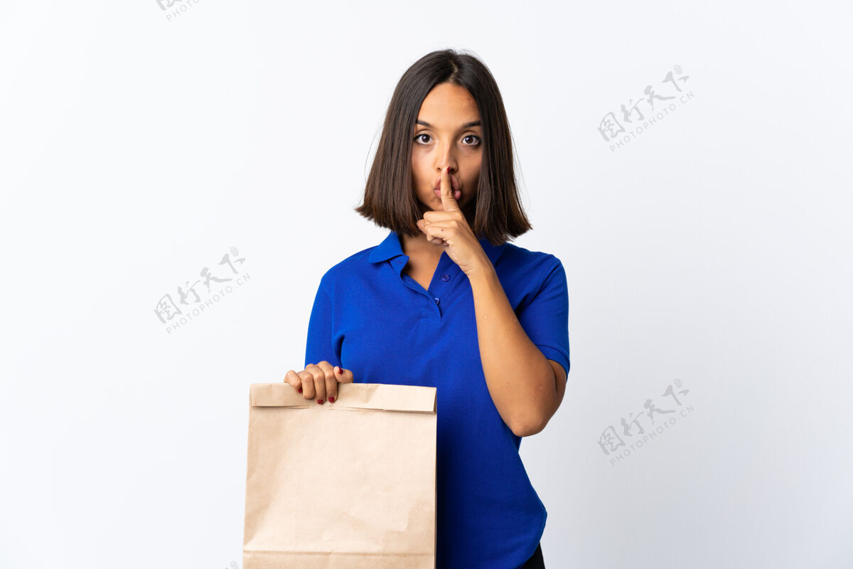 市场一个年轻的拉丁女人拿着一个杂货店的购物袋 在白色的地板上显示出沉默的手势 把手指放进嘴里深色消费者购买