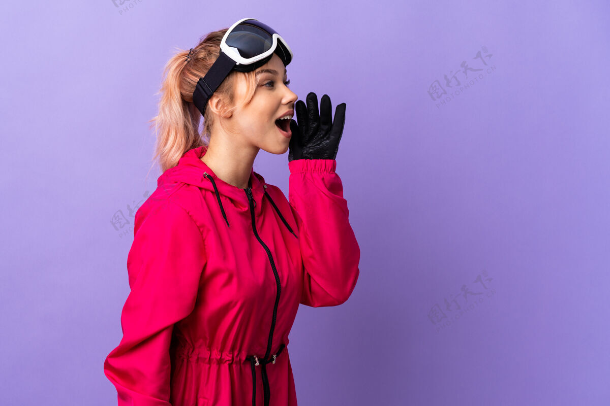 旅行带着滑雪眼镜的滑雪者女孩在孤立的紫色上大声喊叫 嘴巴向一边张开滑雪板喊叫尖叫