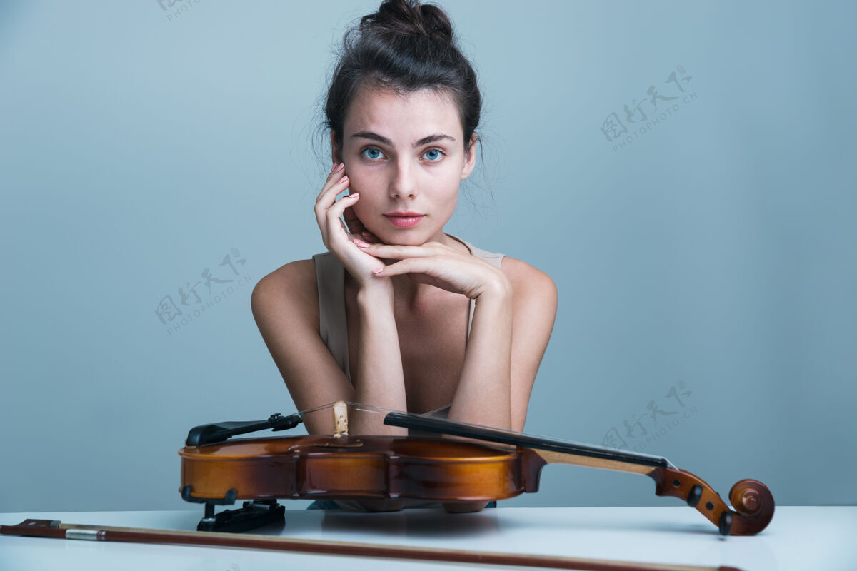 年轻人一个美丽的年轻女子坐在桌子旁 小提琴孤立在蓝色背景下的肖像一小提琴手高加索