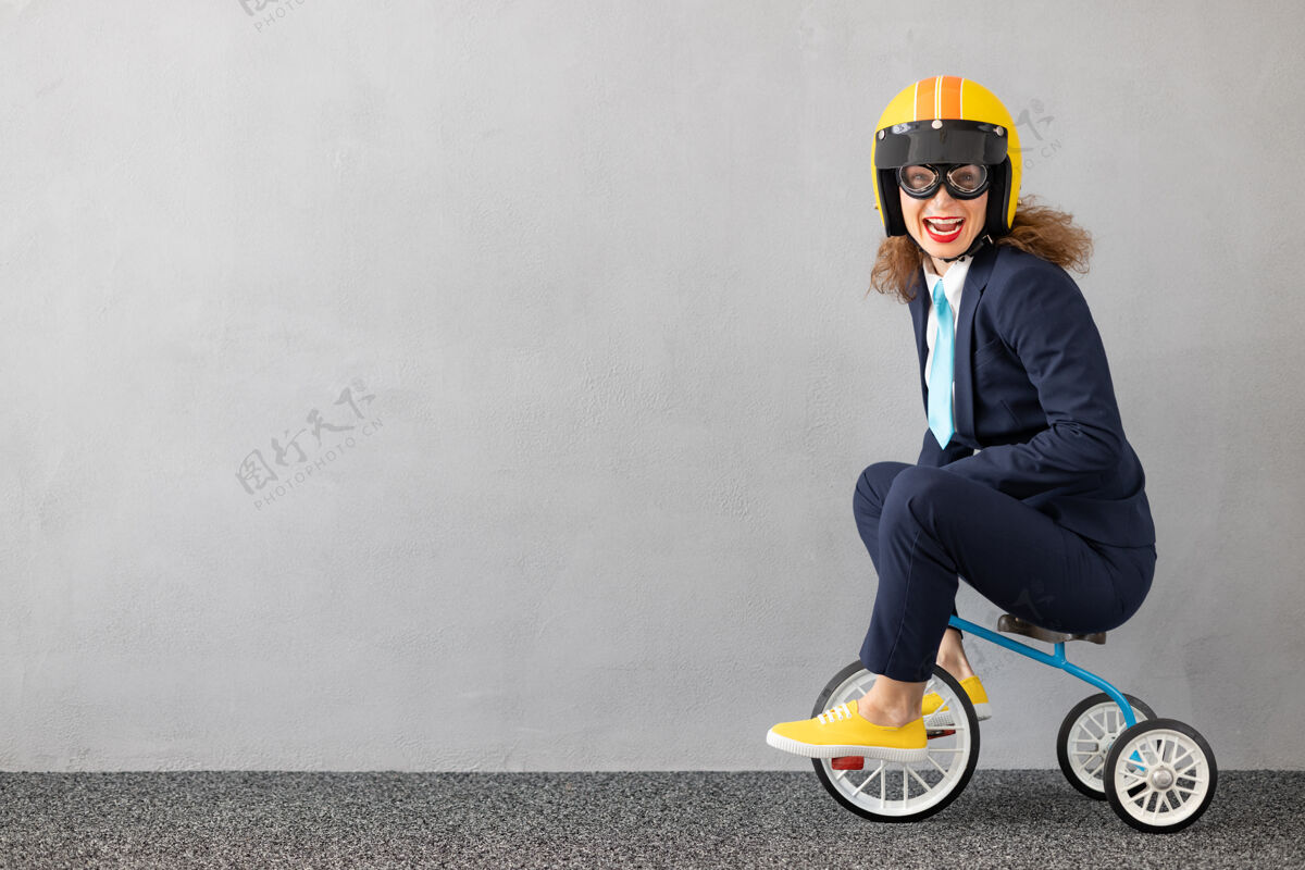自行车成功的女商人在户外驾驶玩具车城市动机西装