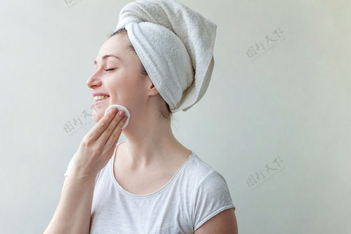 应用头上戴着毛巾的微笑女人的美丽肖像 柔软健康的皮肤 用隔离在白色背景上的化妆棉卸妆触摸皮肤护理制造