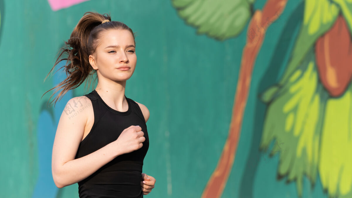 年轻身着运动服的金发女郎在户外训练的路上奔跑 背景是五彩缤纷的墙壁瑜伽运动运动员