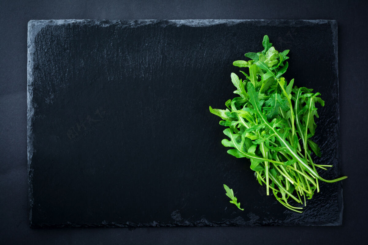 配料一堆新鲜的芝麻菜放在一块黑色的板岩黑板上传统根板岩