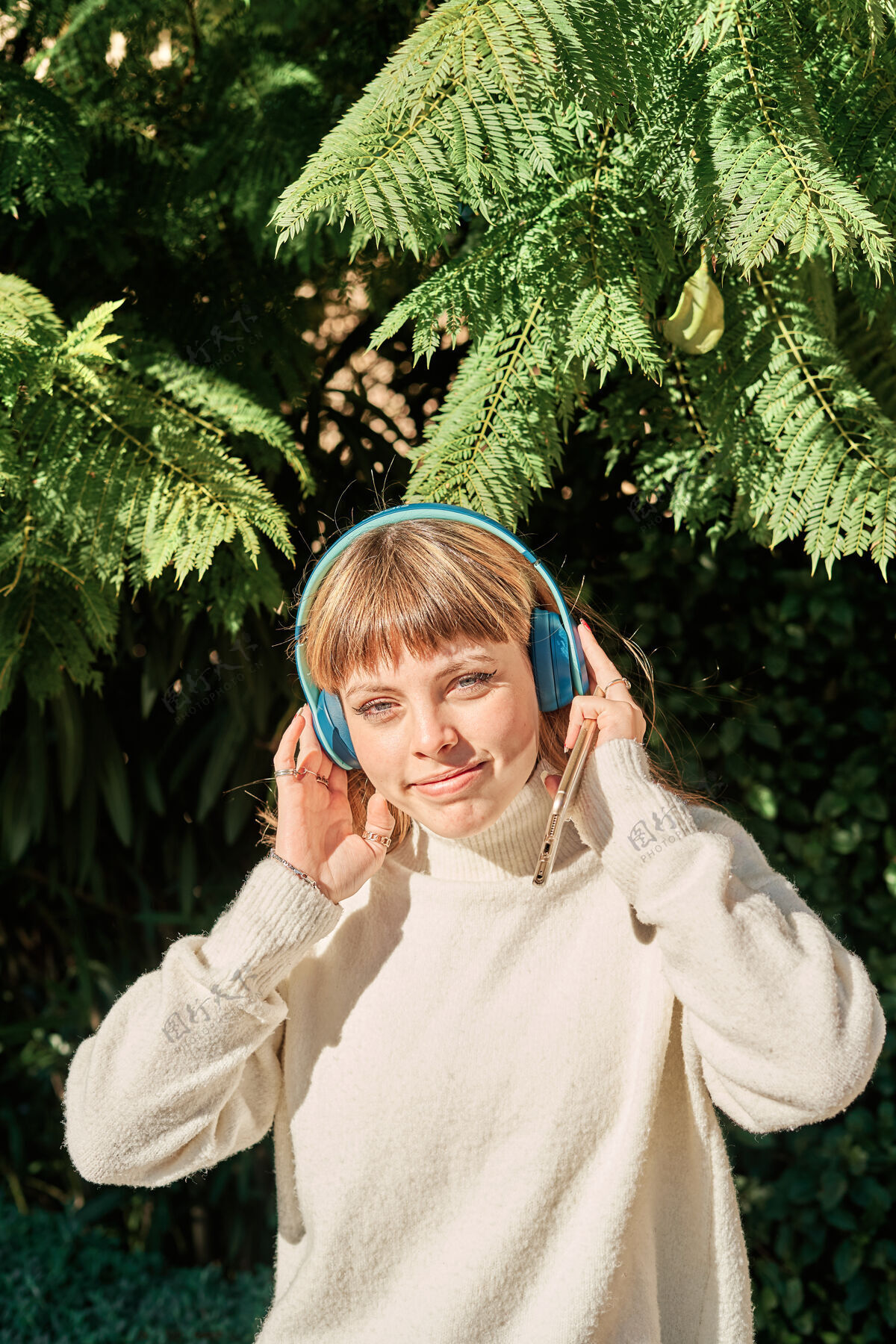 模型一个漂亮的白人女孩在公园里戴着蓝色耳机听音乐成人女人姿势
