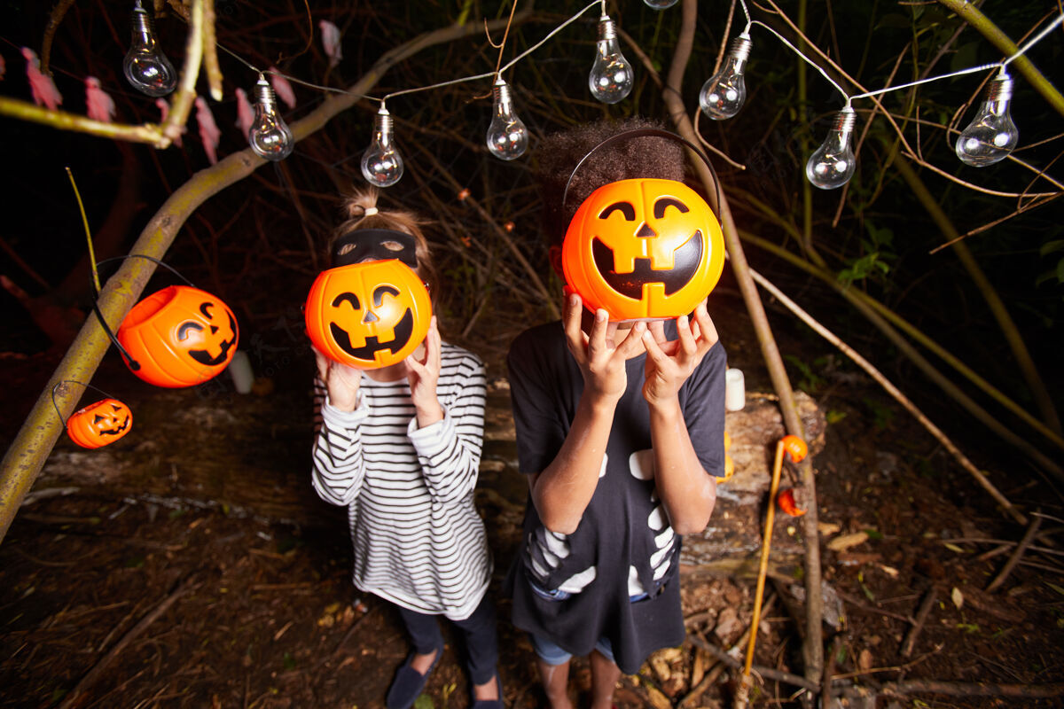 幽灵万圣节派对上 两个孩子站在黑暗的户外 脸前拿着玩具南瓜的画像魔术橙色聚会社交活动