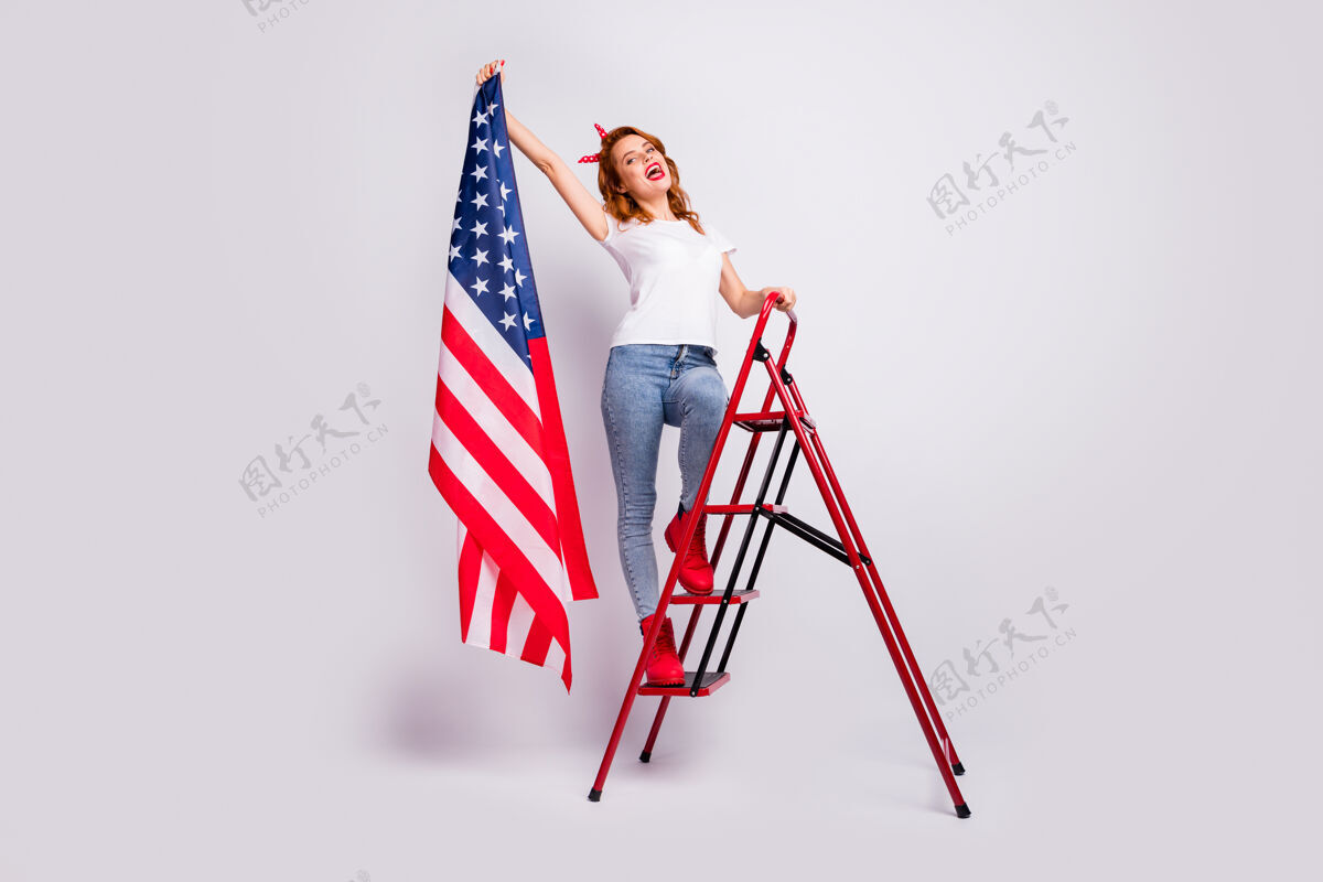 女人全身尺寸她美丽迷人开朗兴奋的幸运女孩站在梯子上手拿美国国旗隔离在浅白色粉彩墙上美国光公民