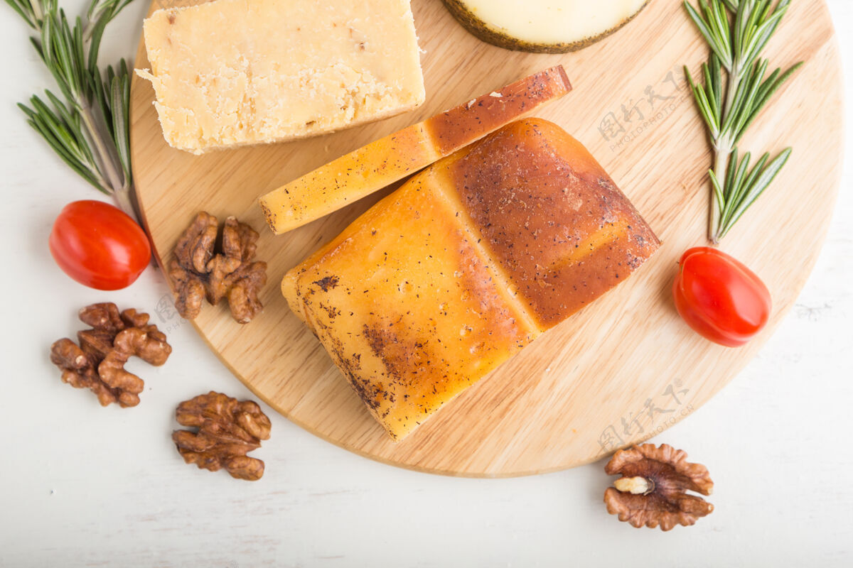 小吃烟熏奶酪和各种奶酪与迷迭香和西红柿在木板上的白色木质表面牛奶自然桌子