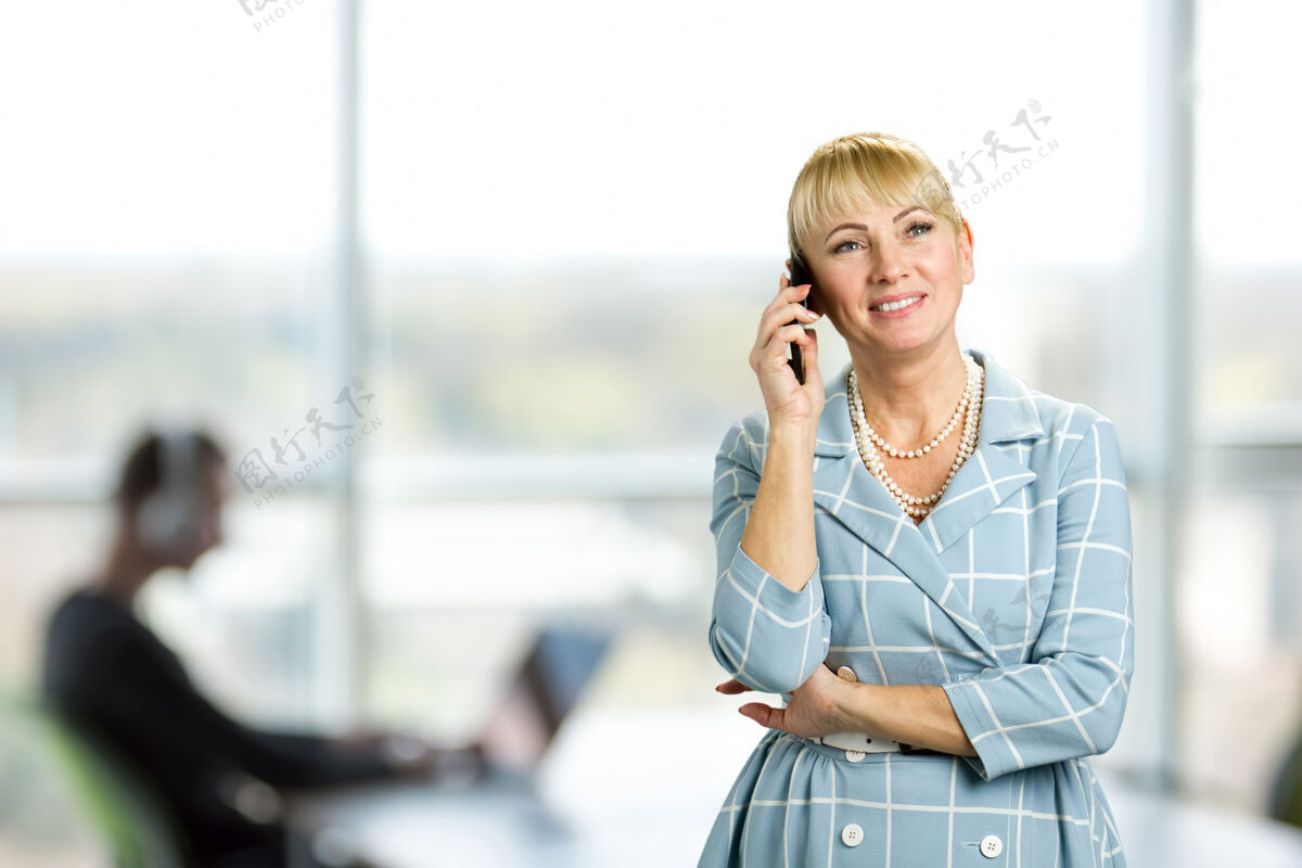 积极快乐的成熟女人在打电话快乐的成熟女人在办公室的窗户上打电话快乐的中年女人在用手机微笑高管电话