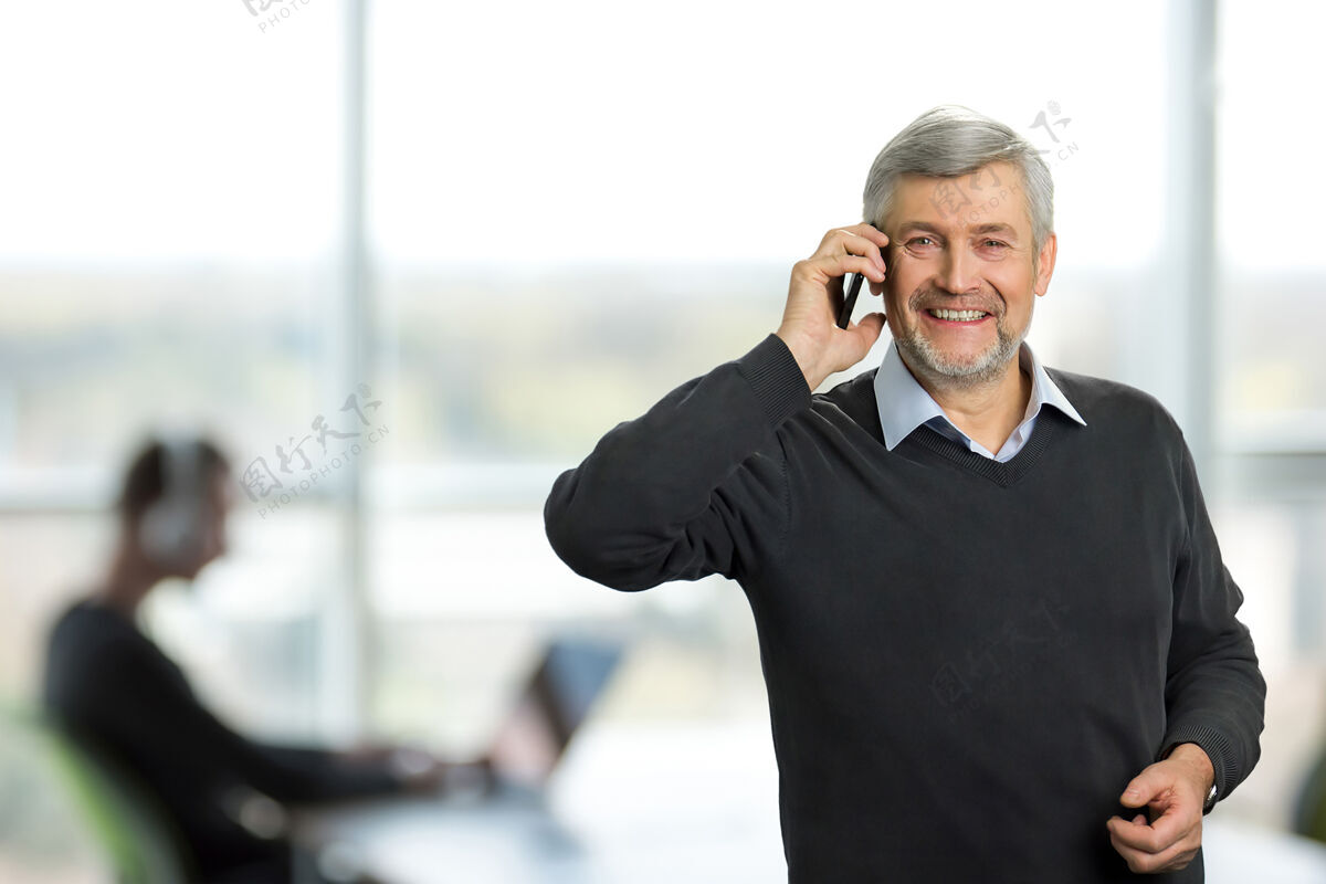 办公室办公室里成熟的男人办公室里快乐的白发男人在讲电话带着手机微笑的老人心理聪明微笑